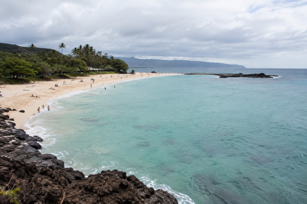 A wide sandy beach on Oahu with calm turquoise water and palm trees along the shore