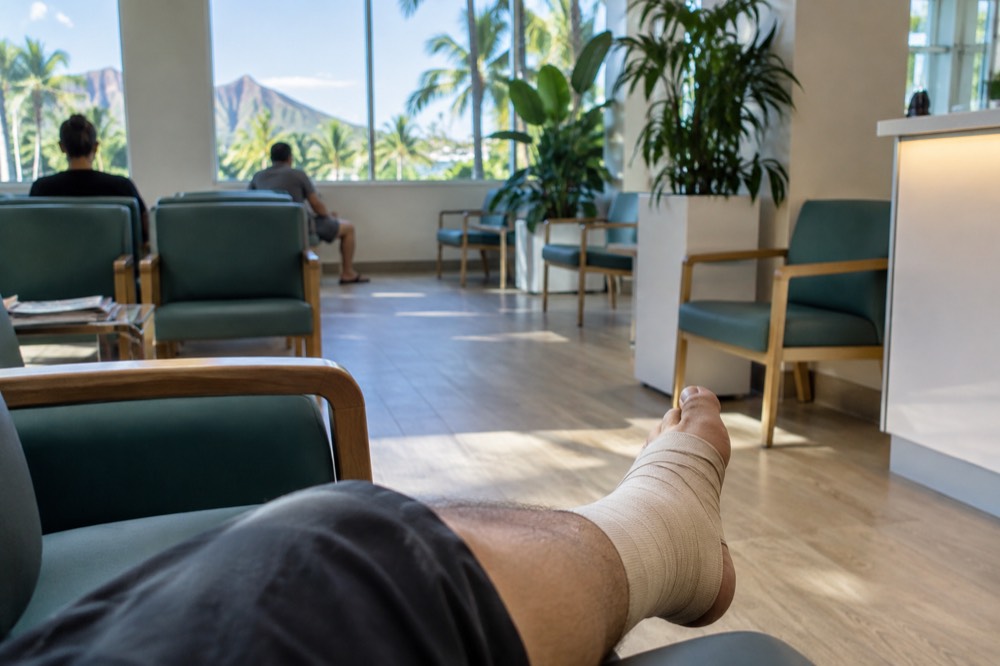 A visitor with a wrapped ankle sitting in a bright clinic waiting area near Waikiki