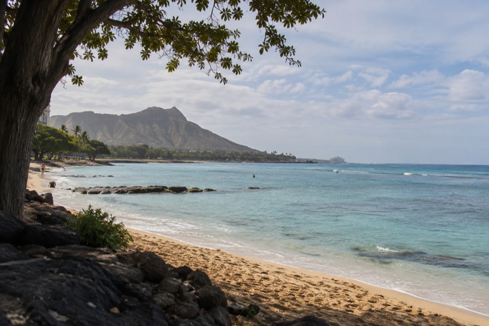 A quiet stretch of Oahu coastline with turquoise water and green hills in the distance