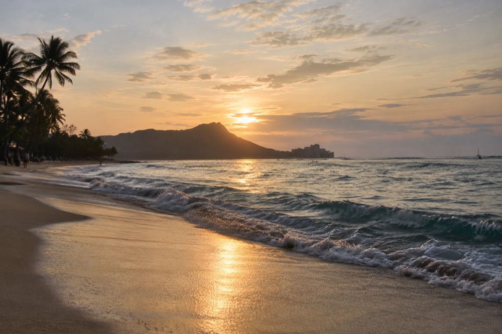 A quiet Oahu beach at golden hour with gentle waves breaking on the sand