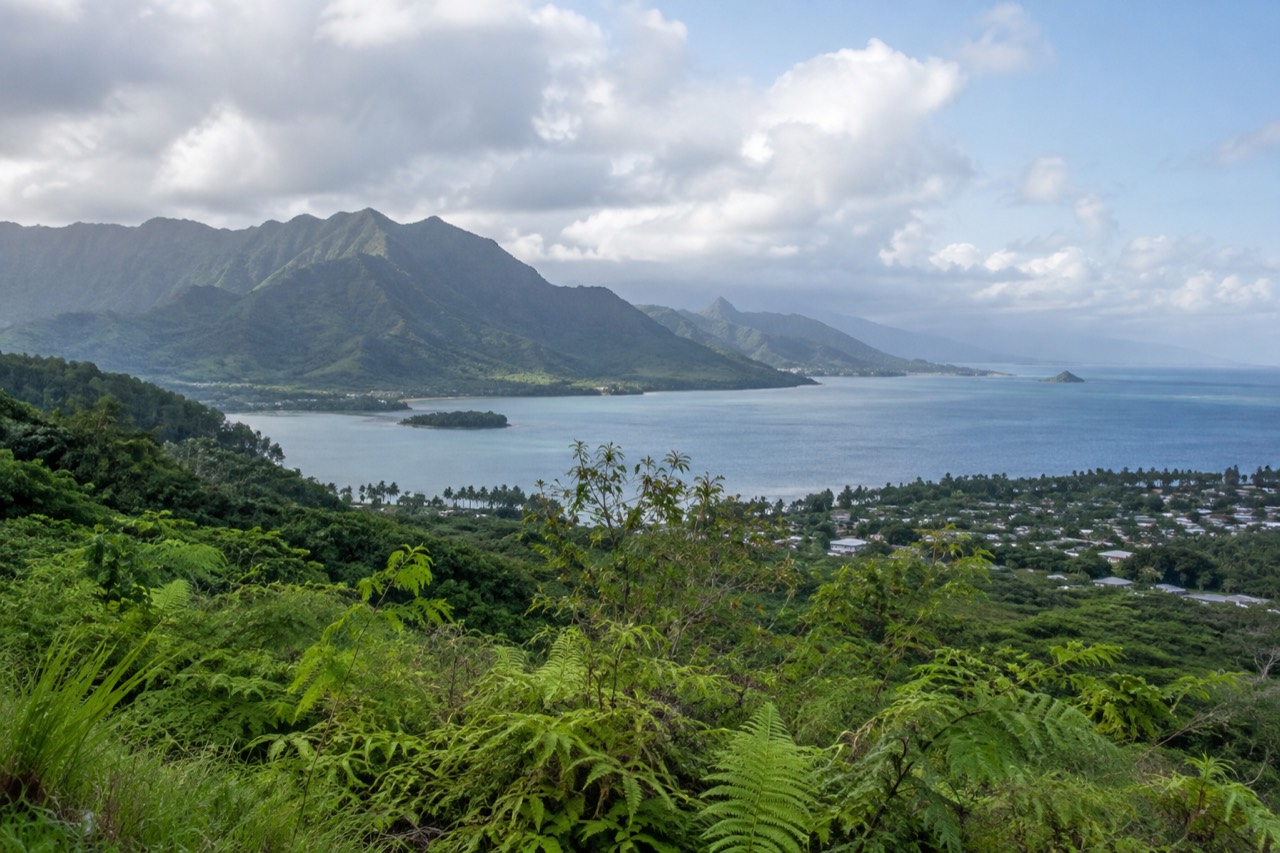 A wide view of Oahu's windward coast with green mountains meeting a calm blue bay