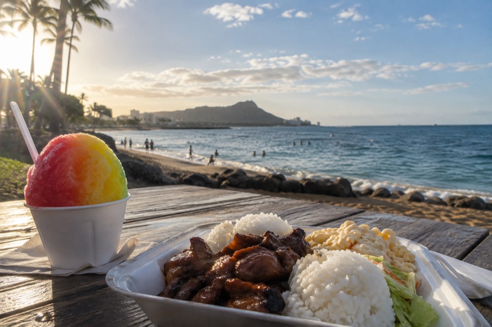 A plate lunch and shave ice on a table overlooking a windward Oʻahu beach