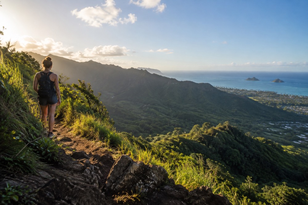 A hiker on a ridge trail looking out over Oahu's green windward valleys toward the ocean