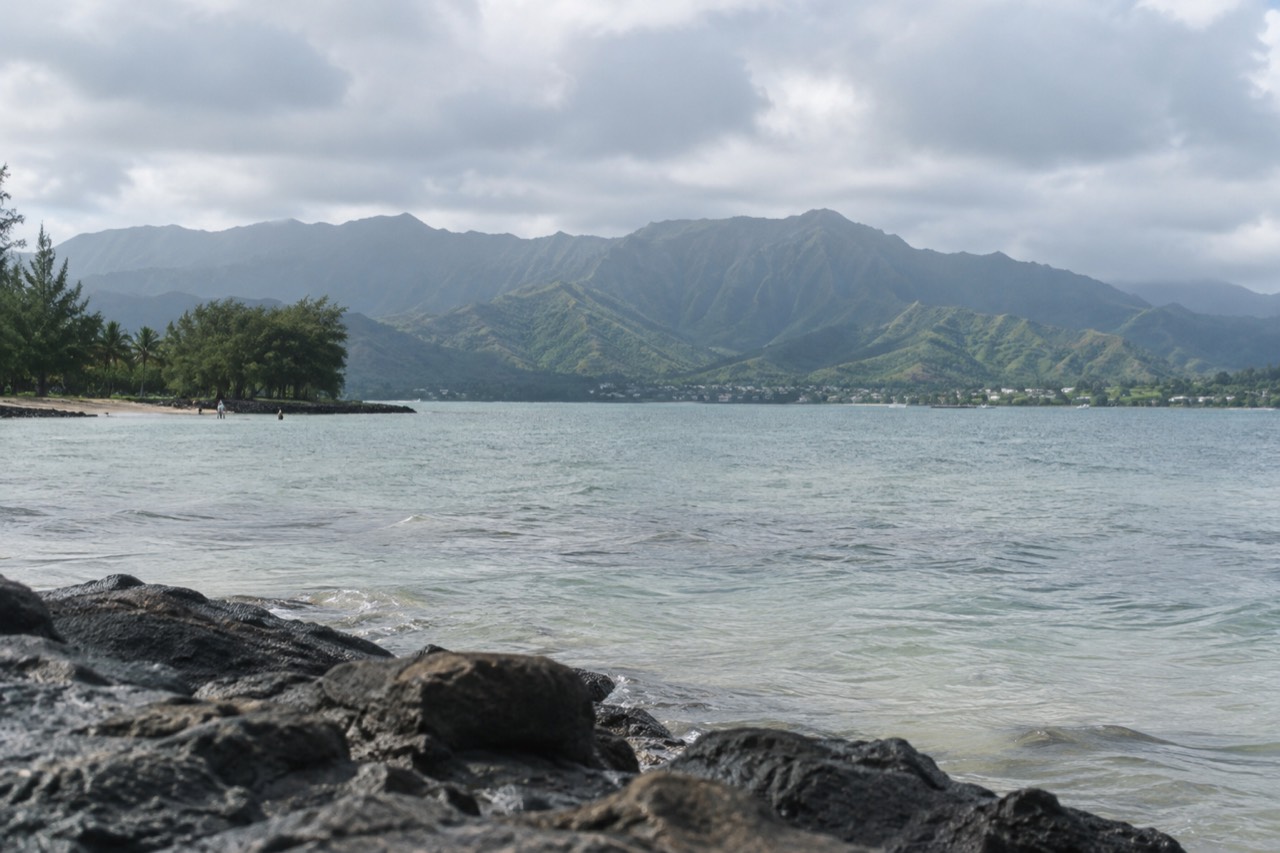 A wide view of Oahu's windward coast with green mountains rising behind a calm bay