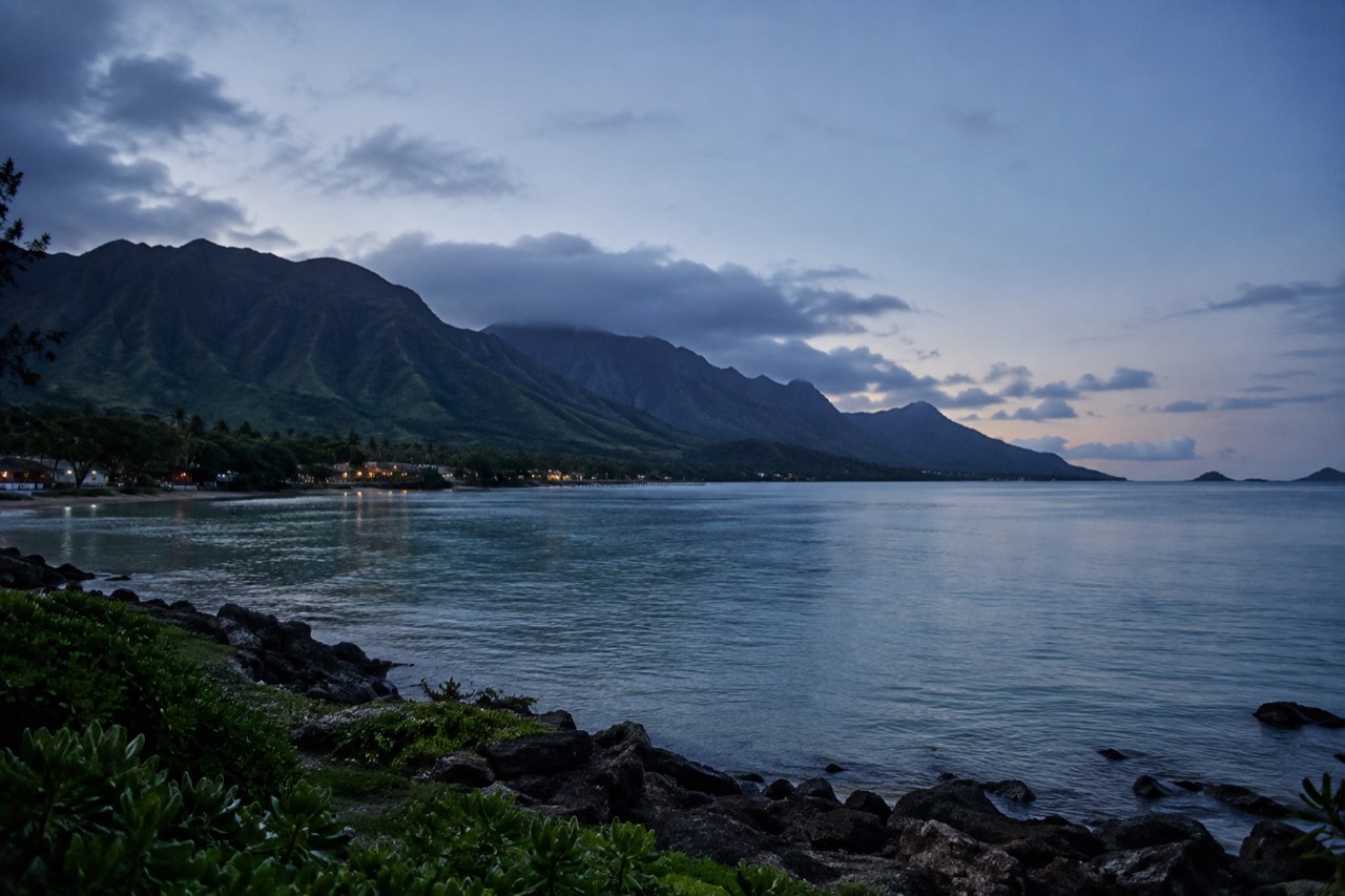 A wide view of Oahu's windward coast with green ridges meeting a calm blue bay