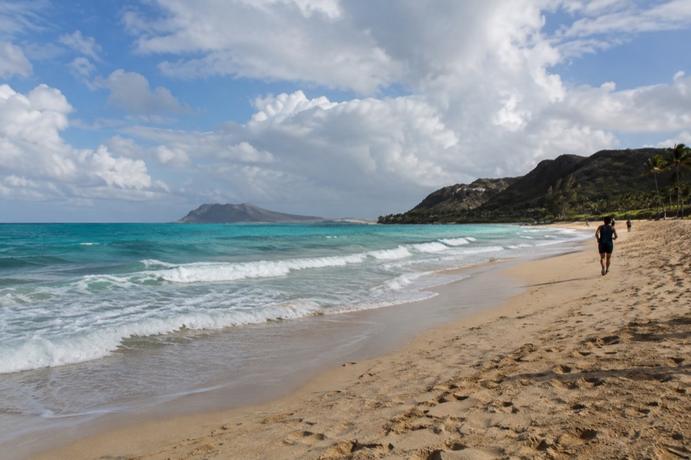 A wide view of Oahu coastline with waves breaking along a sandy beach at midday