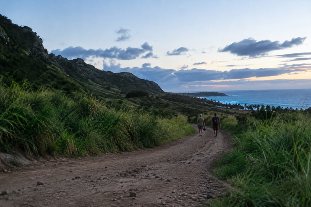 A dusty dirt track running through green hills on Oahu's North Shore under a bright sky