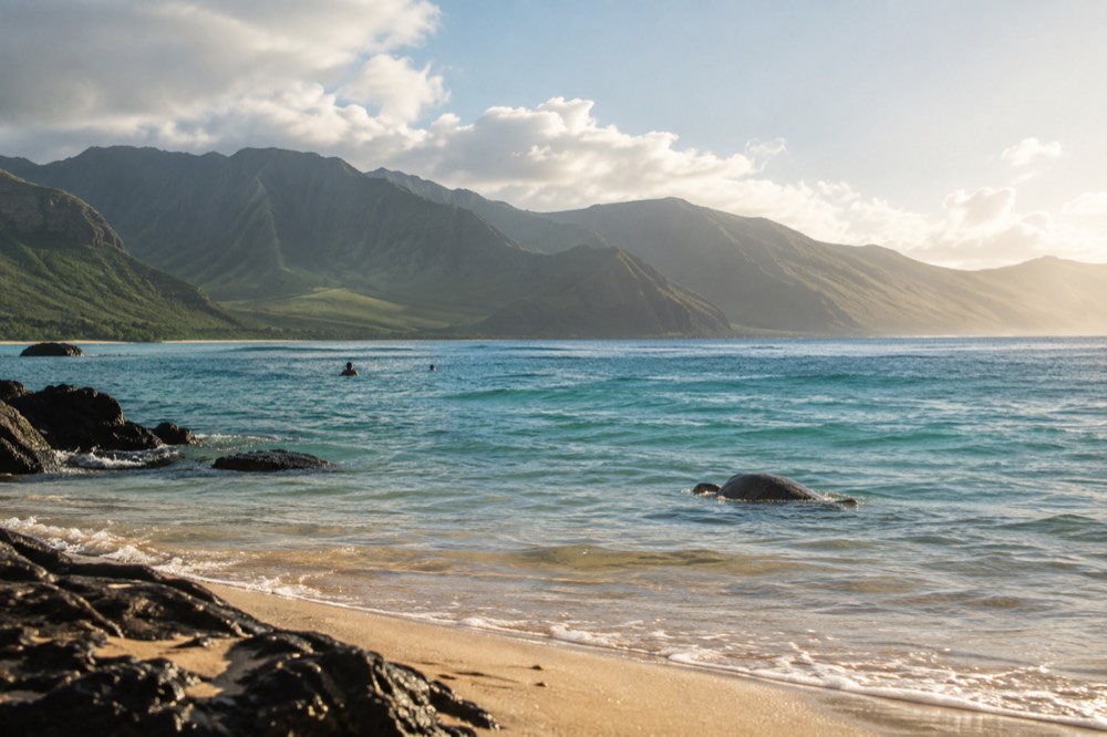 Calm turquoise water over a sandy bottom at an uncrowded windward Oahu beach with the Koʻolau mountains in the background