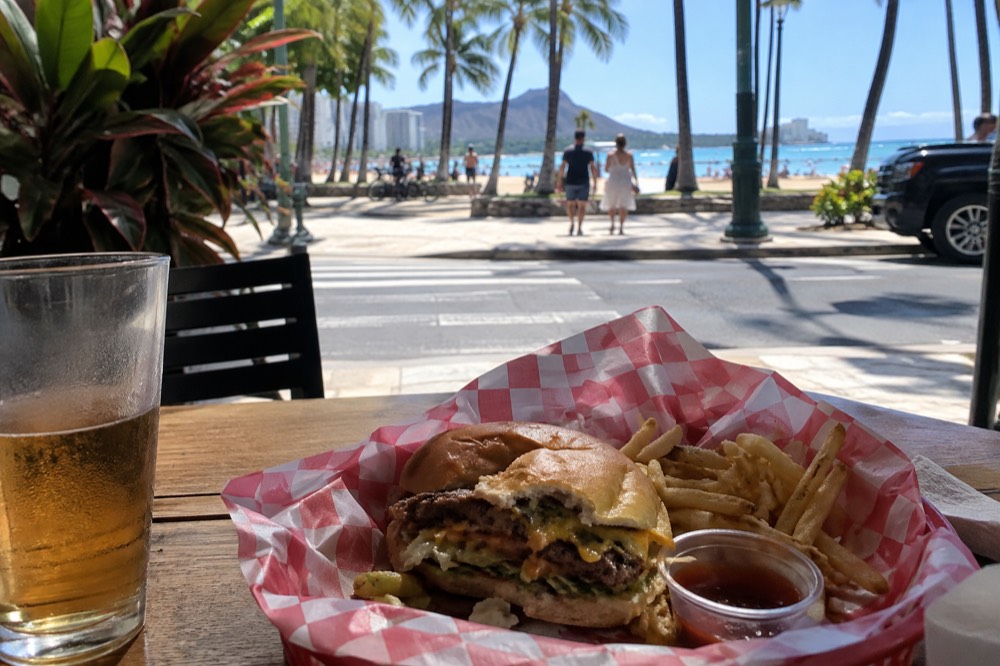 A burger basket with fries eaten at an outdoor table near a beach town street