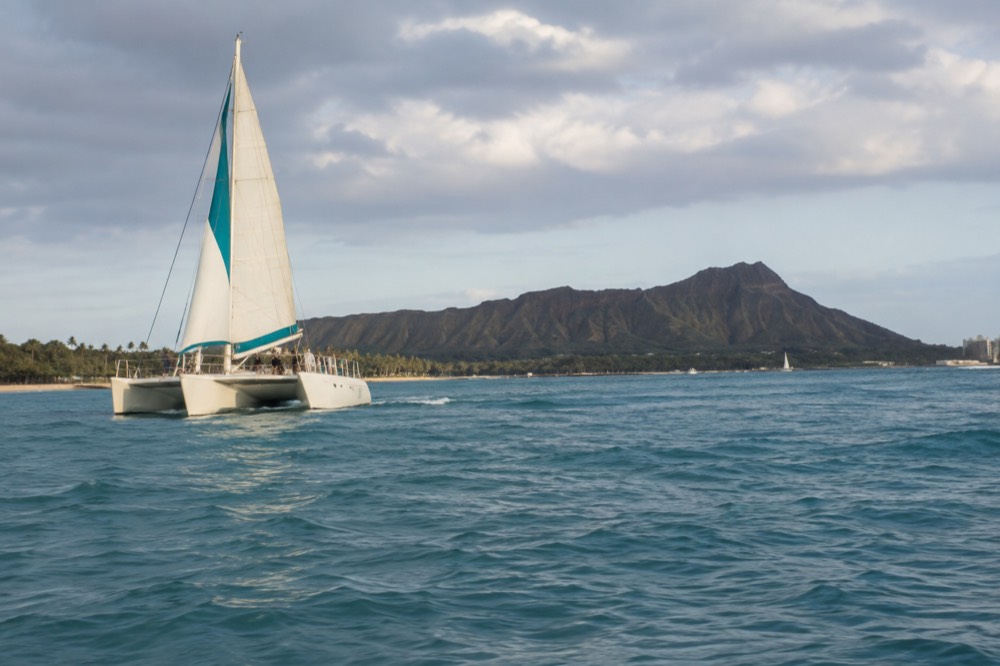 A catamaran sailing along the Waikiki coastline of Oahu toward Diamond Head in late afternoon light