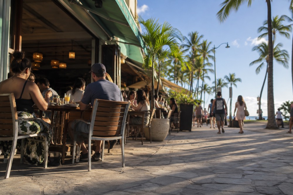 A busy sidewalk lunch counter with customers eating at outdoor tables in a Honolulu neighbourhood
