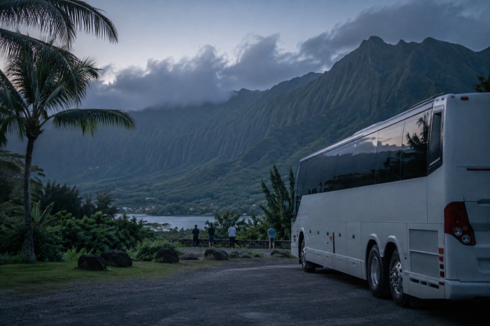 A tour bus parked beside a green valley on Oahu's windward coast with ridged mountains behind it