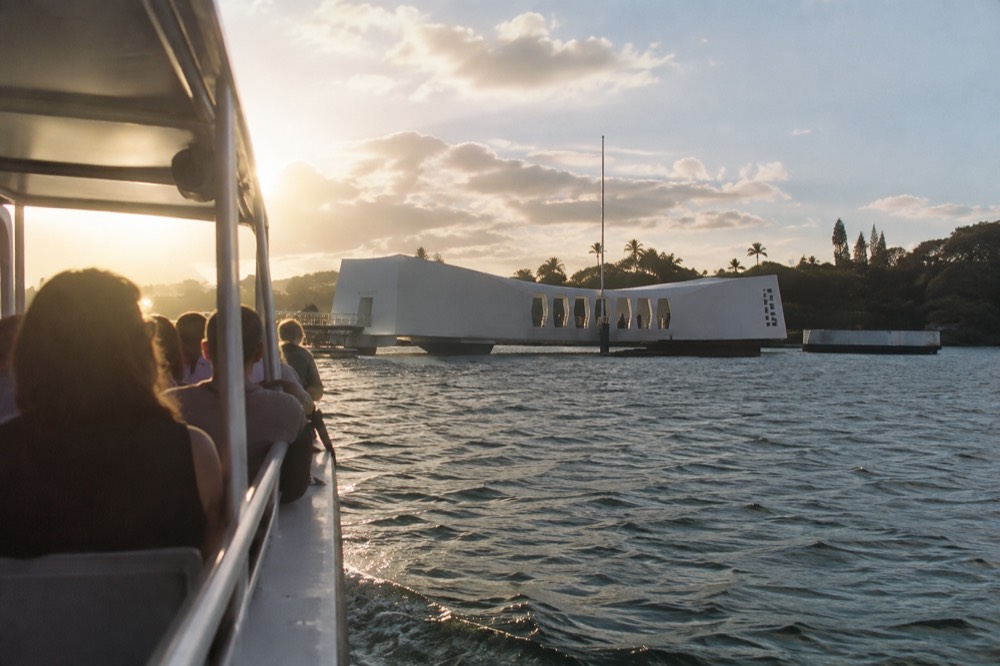 The white USS Arizona Memorial structure resting above the water at Pearl Harbor with a tour boat nearby