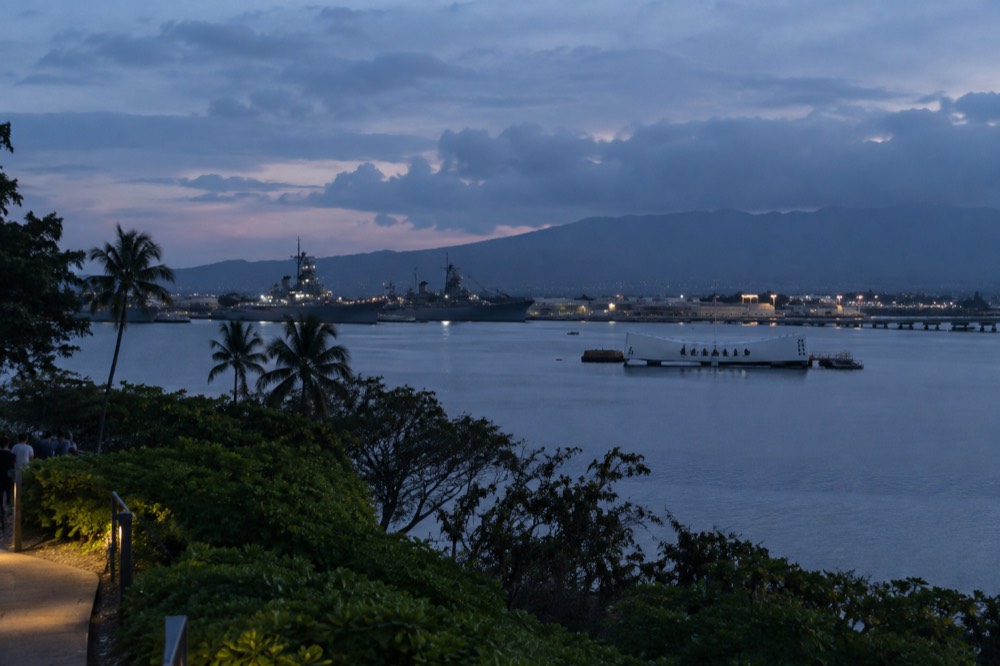 View across Pearl Harbor toward the USS Arizona Memorial with navy ships moored in the distance