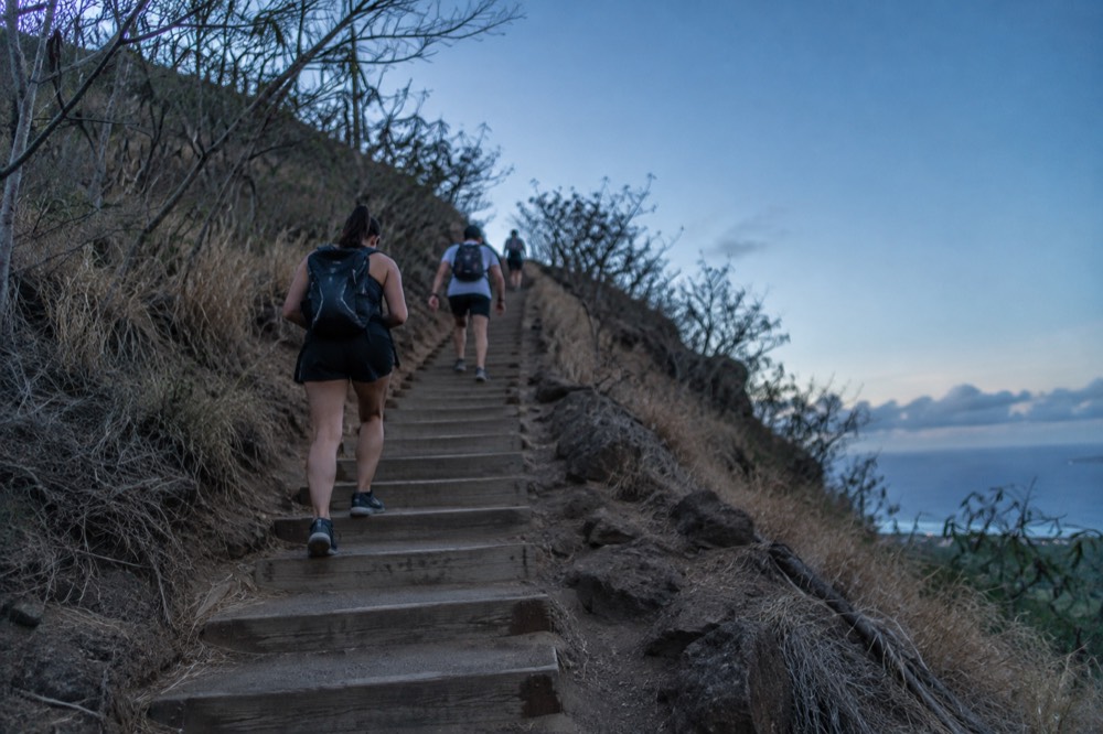 Hikers climbing a long flight of weathered steps cut into a dry hillside under a clear sky