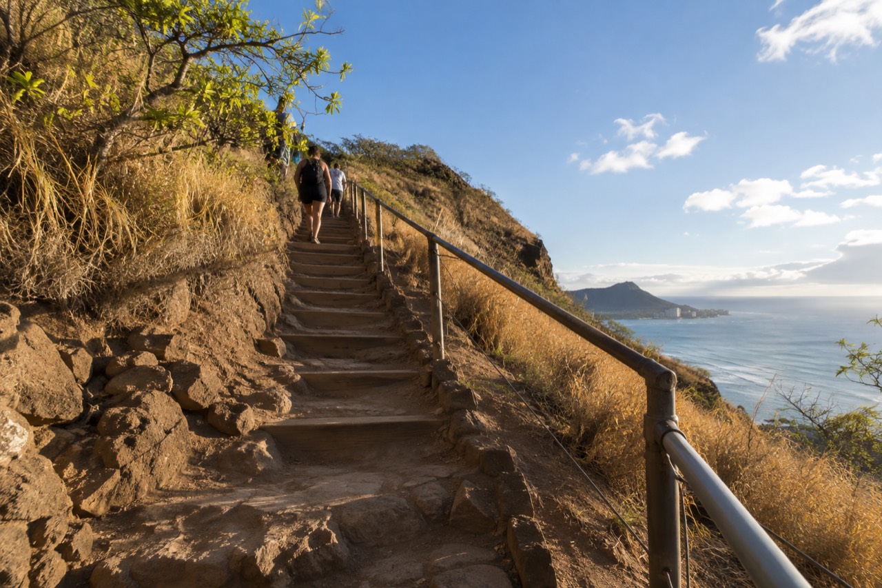 A steep dirt and stair trail rising toward a ridgeline above the Honolulu coastline