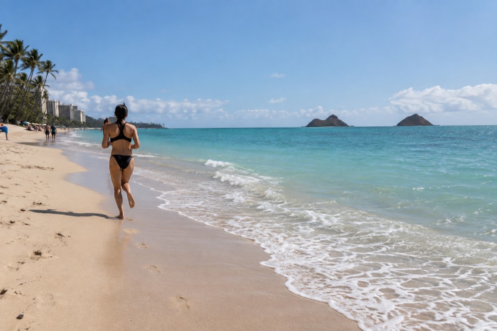 A narrow strip of pale sand beside calm turquoise water with two small islands on the horizon
