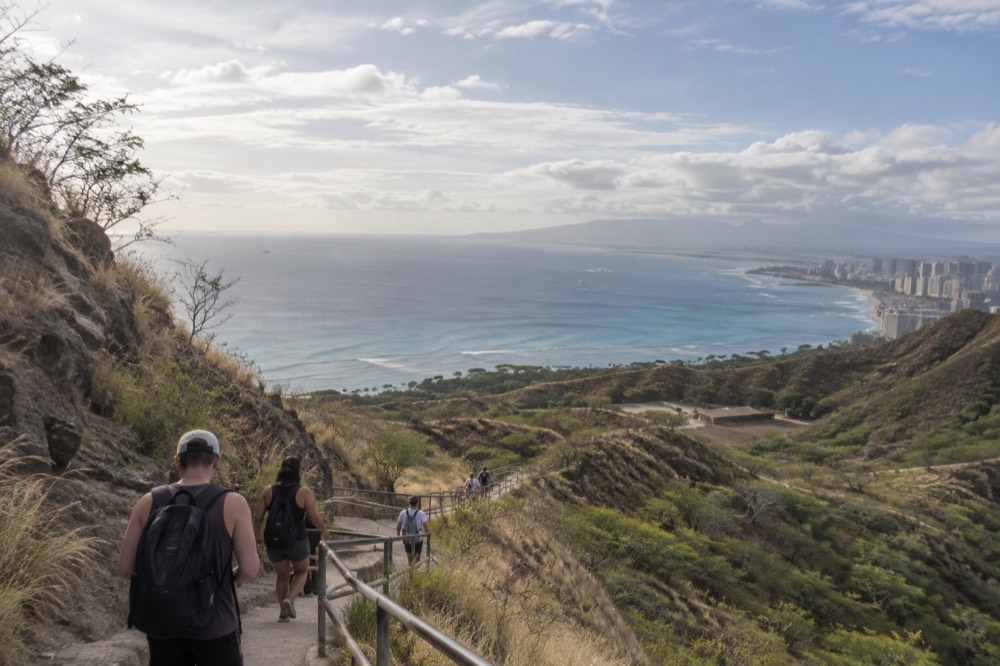Hikers walking the switchback trail inside the Diamond Head crater with the Pacific ocean in the distance