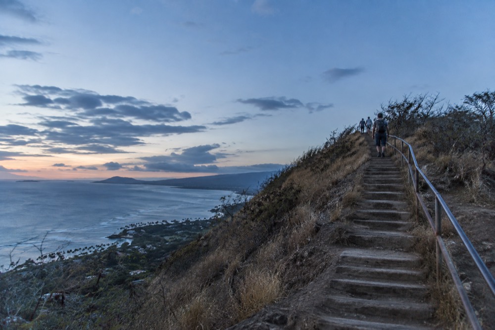 A steep staircase trail climbing a dry ridgeline above the Honolulu coastline