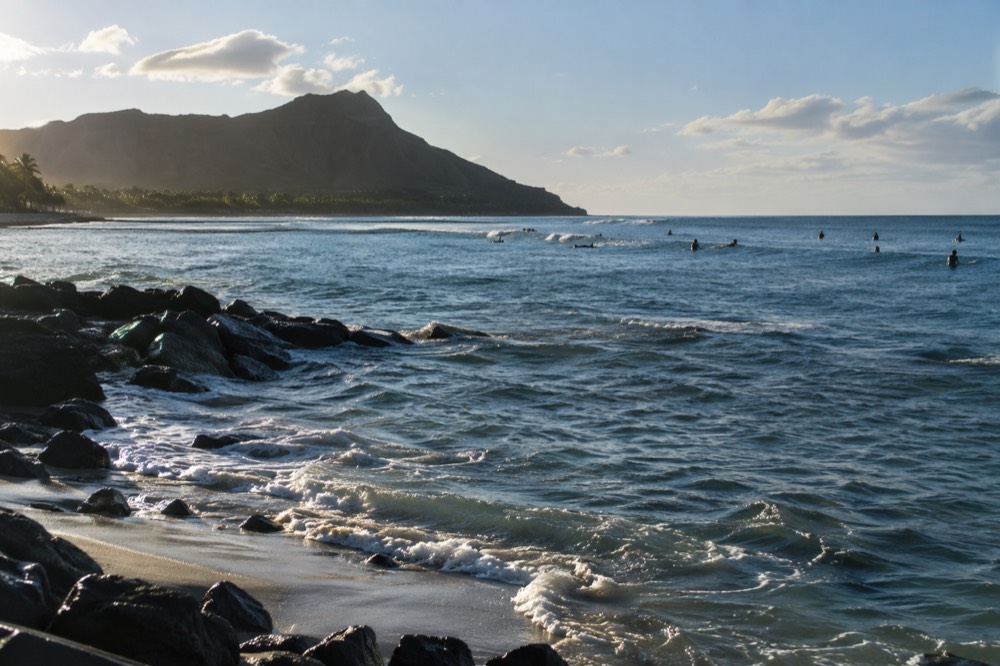 Surfers sitting on their boards beyond a reef at the quiet Diamond Head end of Waikīkī beach