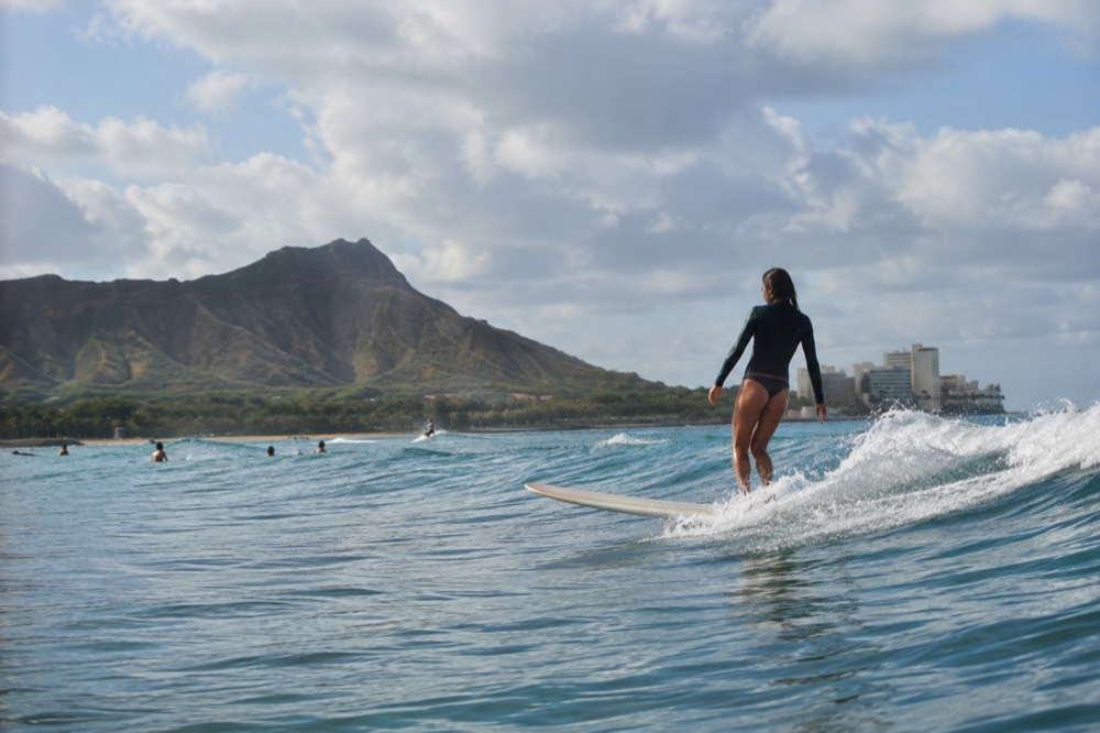 A longboarder riding a gentle rolling wave at the Diamond Head end of Waikīkī with the crater in the background
