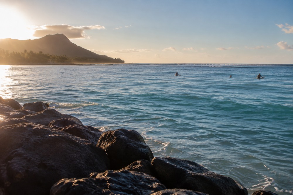 A calm turquoise lagoon on Oahu with gentle waves breaking on a distant reef line under a clear sky
