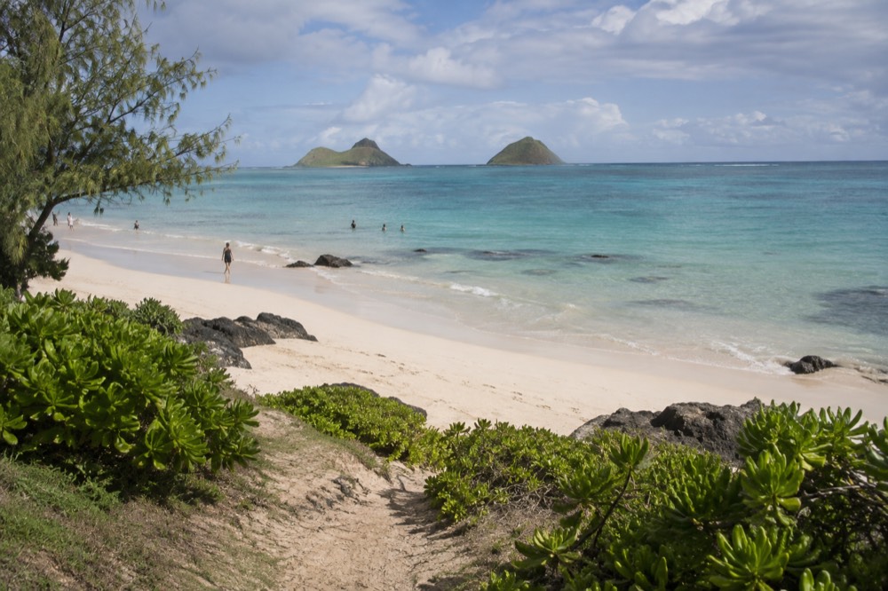 A calm bay with shallow turquoise water and distant offshore islands seen from a sandy beach