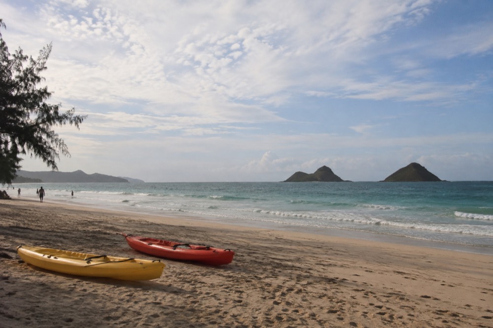 Kayaks resting on a wide beach with small offshore islands on the horizon