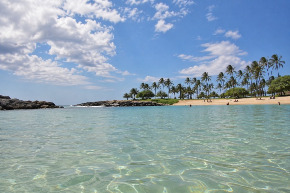 Calm turquoise lagoon water at Ko Olina with a sandy beach and palm trees under a clear sky