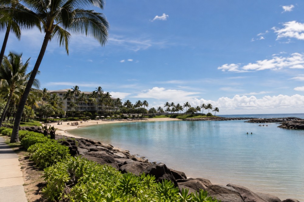 A resort lagoon at Ko Olina seen from a walking path, with calm water and landscaped palms along the shore