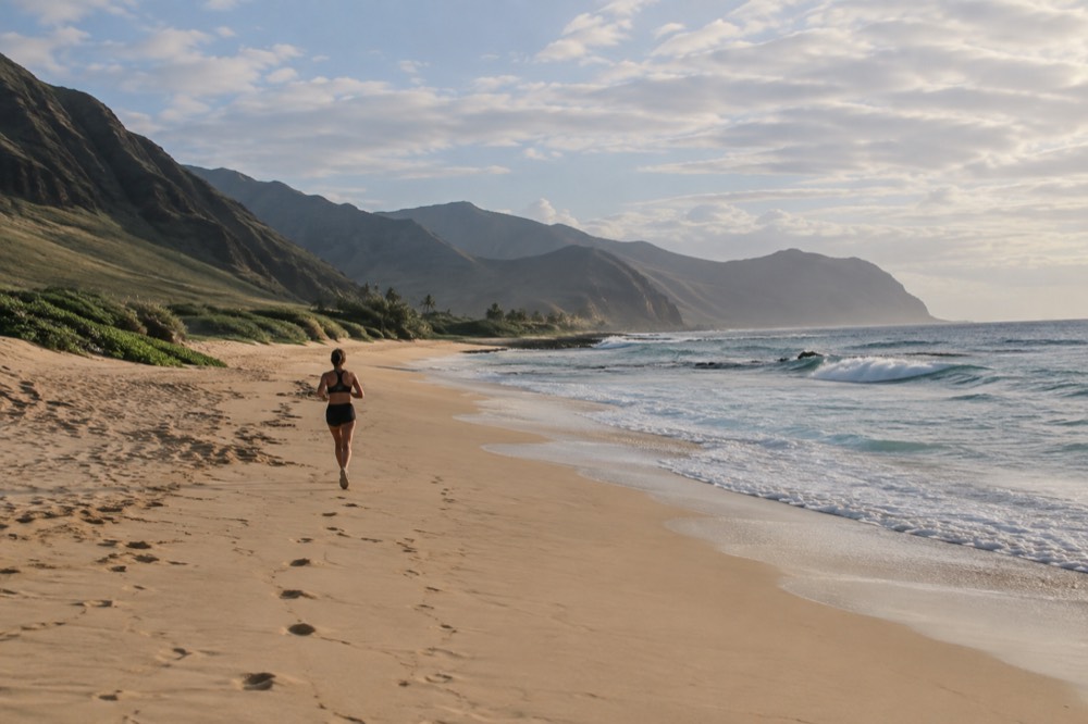 An empty golden sand beach on the western coast of Oahu with low green ridges and a wide sky