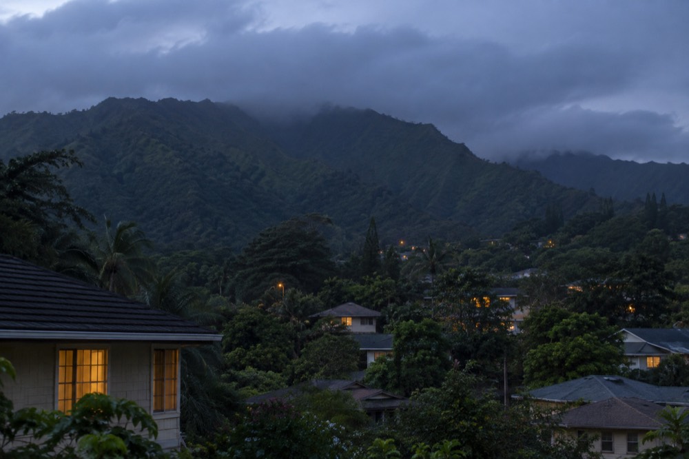 A rainforest valley on Oahu with ridged green mountains rising above rooftops under broken cloud