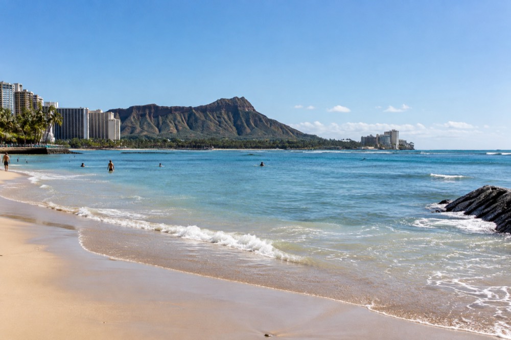 A calm Waikīkī beach with Diamond Head crater in the background under a clear sky