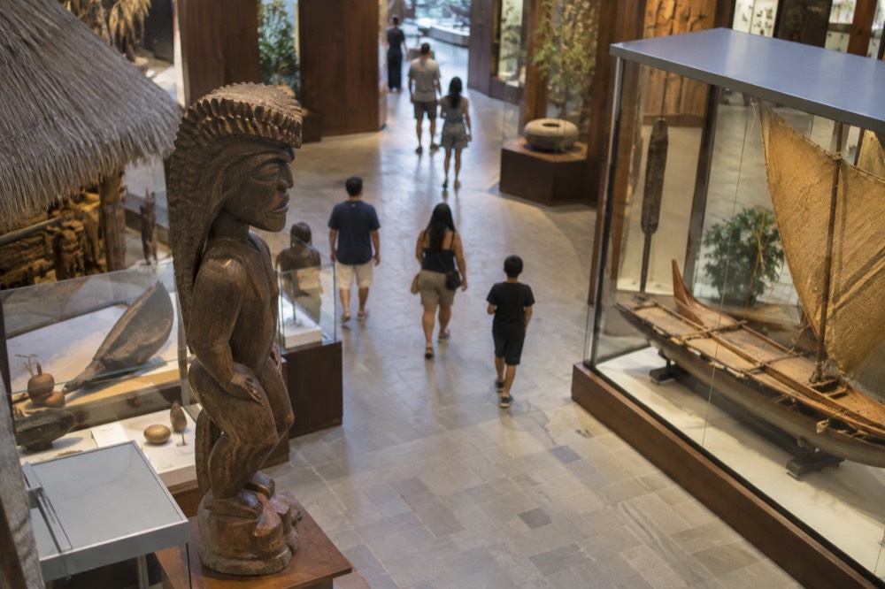 Visitors walking through a bright museum hall displaying Hawaiian artefacts