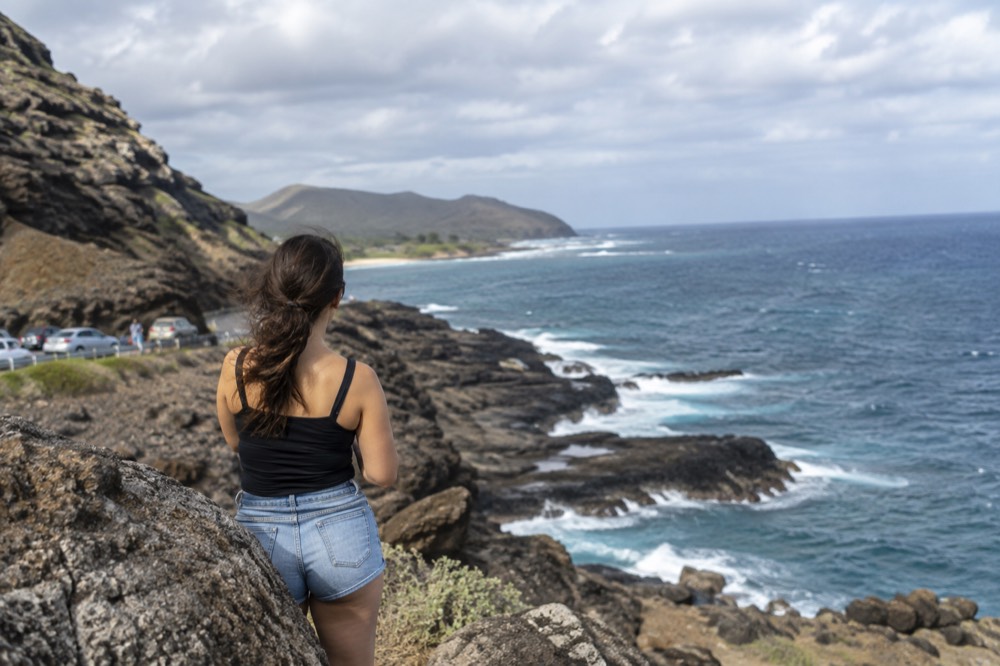 A coastal lookout parking area above a rocky lava shoreline on a sunny morning in Hawaii
