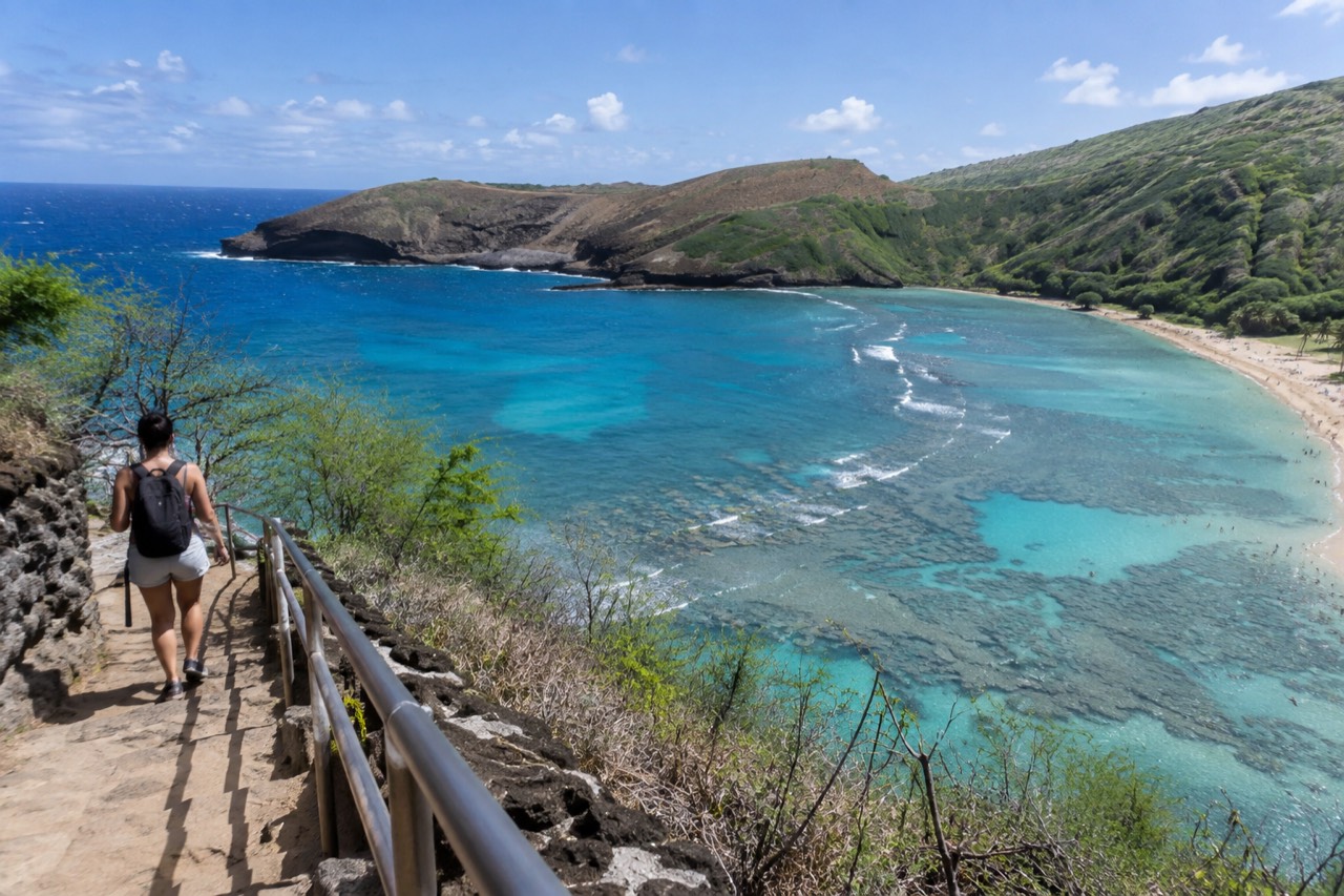 Aerial view of a curved blue bay with reef formations visible through clear water and green hills rising around it