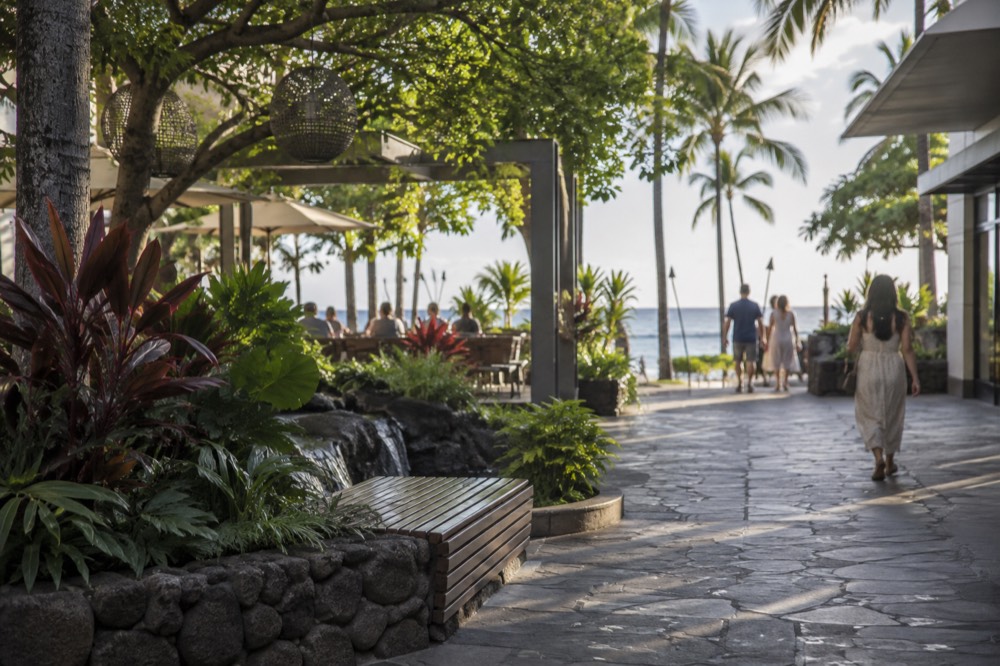 Open-air walkways and tree-shaded seating at a Waikīkī shopping center in the late afternoon