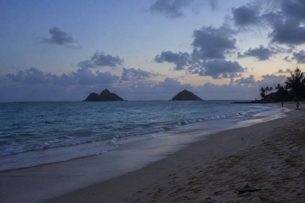 A wide sandy beach on Oahu's windward coast with calm turquoise water and the Mokulua Islands on the horizon