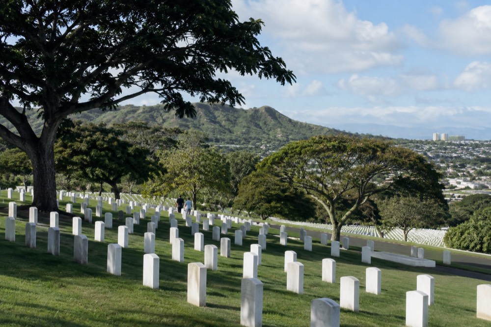 Rows of white grave markers on the green slopes of a volcanic crater cemetery under a blue sky