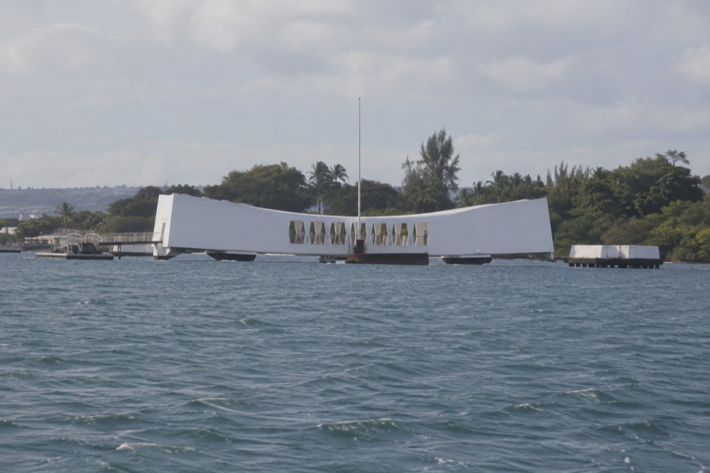The USS Arizona Memorial, a white structure spanning the sunken battleship, seen from the water at Pearl Harbor