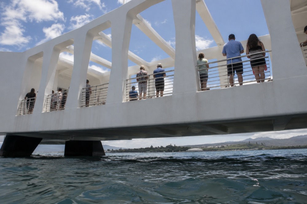 Visitors standing quietly along the open walkway of the USS Arizona Memorial looking down at the water