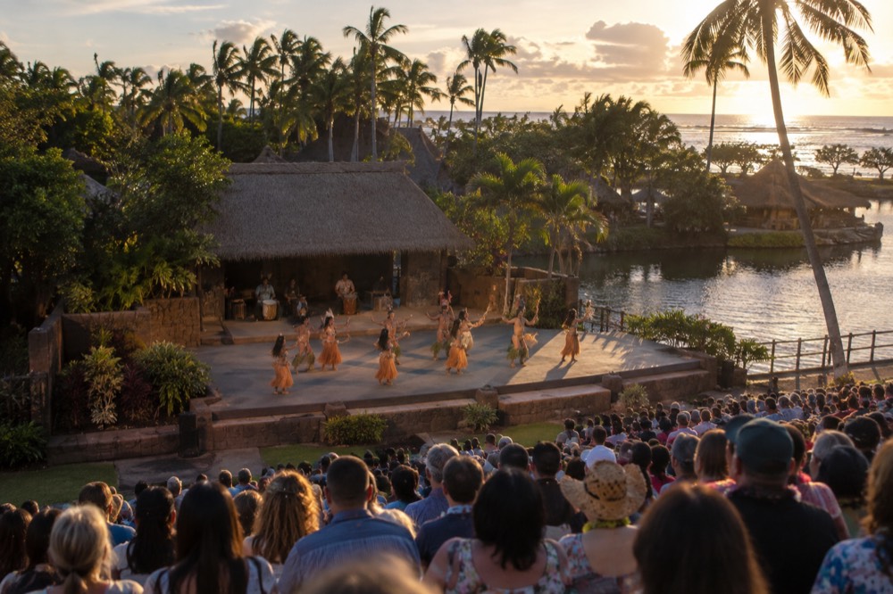 Performers in traditional dress dancing on an outdoor stage in front of a large evening audience