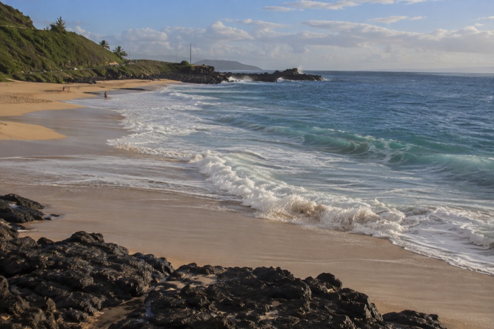 Waves curling onto a steep sandy beach on Oahu's south shore in early morning light