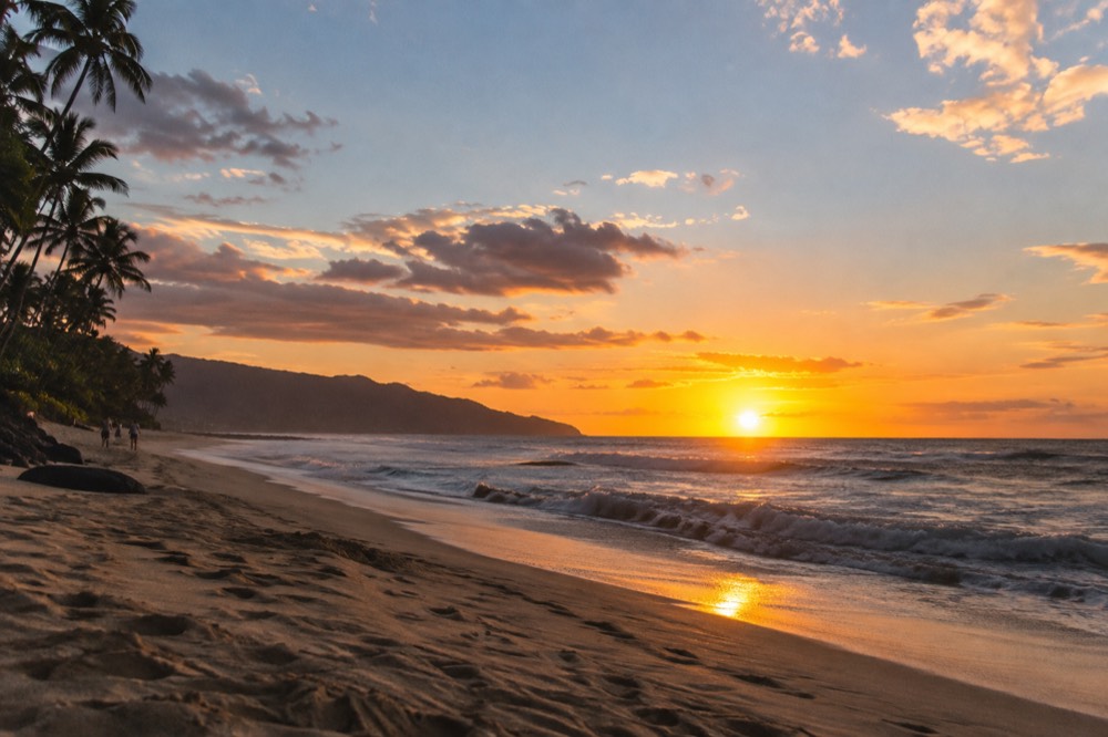 A long stretch of North Shore sand at dusk with a low sun over the water