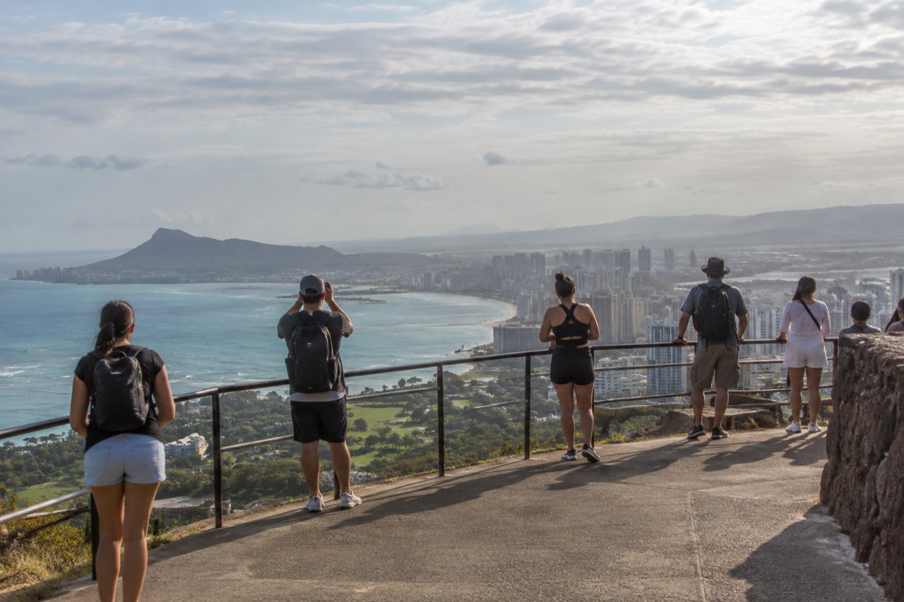 A paved lookout platform above Honolulu with the city skyline and Diamond Head crater in the distance under a late afternoon sky