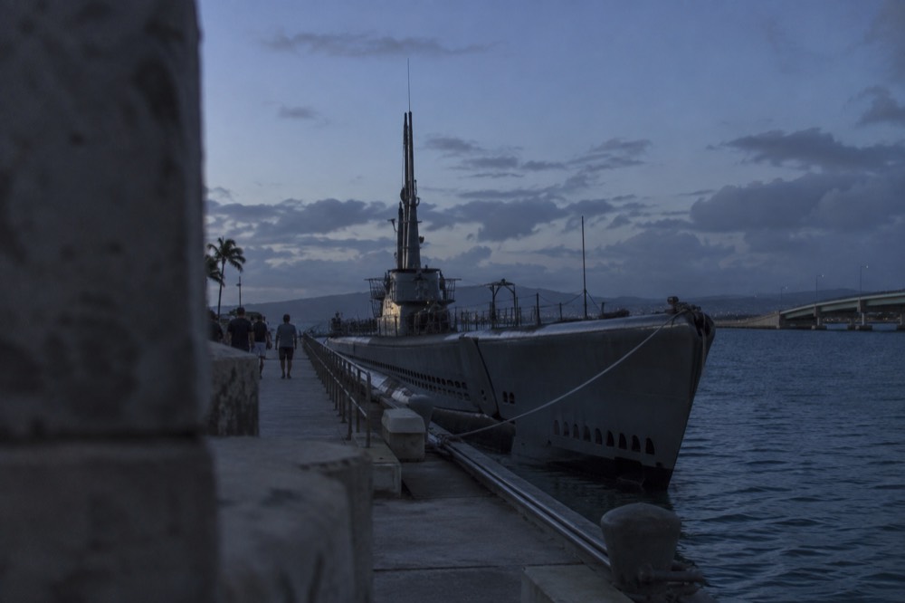 A grey fleet submarine moored at a waterfront dock with visitors walking along the pier