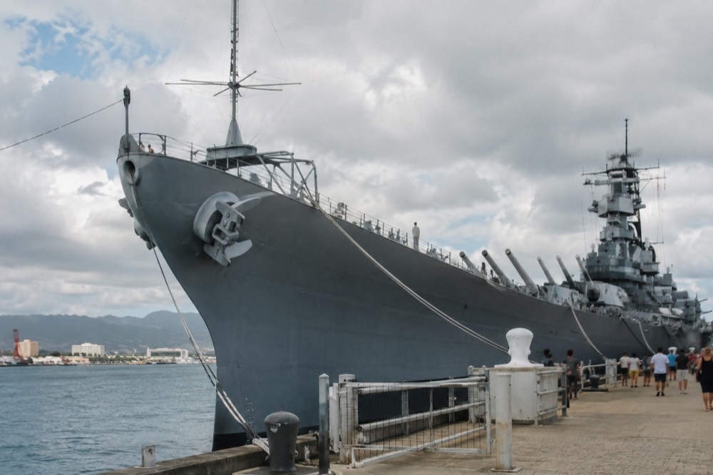 The bow of the battleship USS Missouri rising above the walkway at Ford Island, with visitors on the deck below