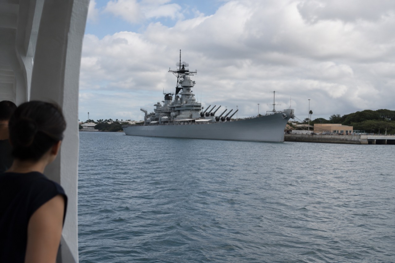 The grey hull of the battleship USS Missouri moored at Ford Island in Pearl Harbor under a partly cloudy sky