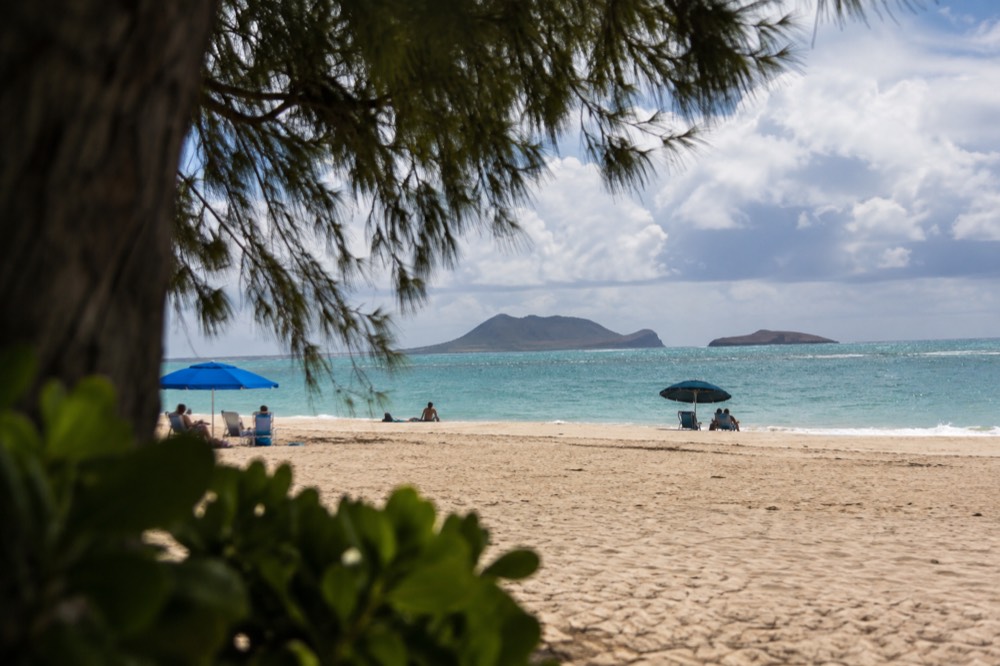 Wide sandy beach at Waimanalo with calm turquoise water and a few scattered beach umbrellas