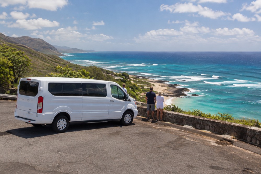 A tour van parked at a coastal lookout on Oahu with turquoise water below